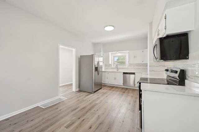 kitchen featuring decorative backsplash, appliances with stainless steel finishes, white cabinets, a sink, and visible vents