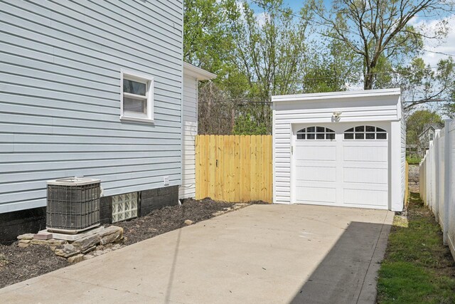 detached garage featuring fence, concrete driveway, and central air condition unit