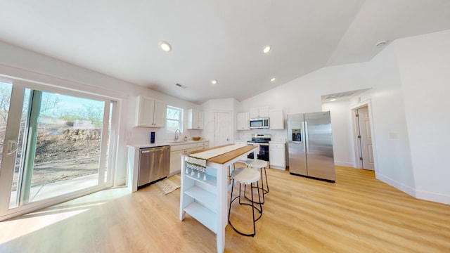 kitchen with white cabinets, a kitchen breakfast bar, stainless steel appliances, open shelves, and a sink