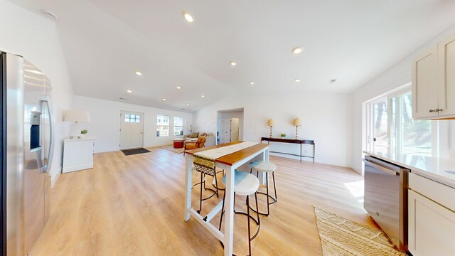 kitchen featuring white cabinets, stainless steel appliances, lofted ceiling, and light wood-type flooring