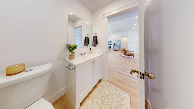 bathroom with toilet, lofted ceiling, vanity, and wood finished floors