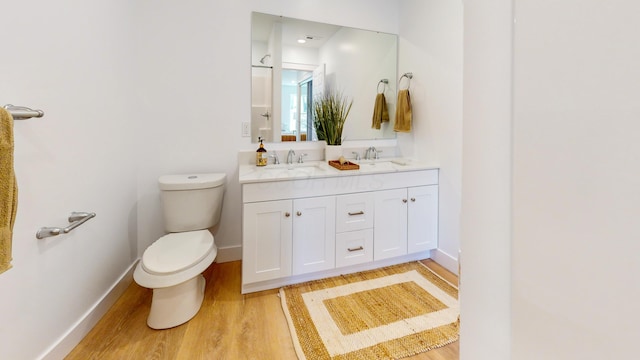 bathroom with double vanity, wood finished floors, toilet, and a sink