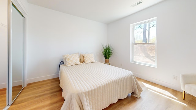 bedroom featuring a closet, light wood-style floors, visible vents, and baseboards