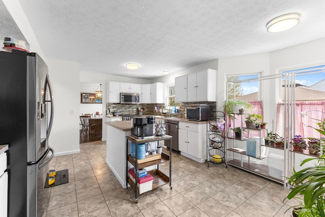 kitchen with light tile patterned floors, backsplash, white cabinets, and stainless steel appliances