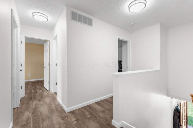 hall with visible vents, wood finished floors, baseboards, a textured ceiling, and an upstairs landing