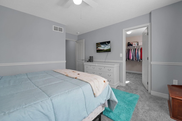 bedroom with a spacious closet, ceiling fan, light colored carpet, baseboards, and visible vents