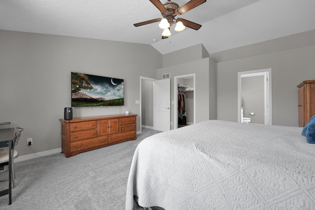 bedroom with a walk in closet, connected bathroom, light carpet, baseboards, and lofted ceiling
