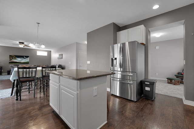 kitchen featuring a center island, dark stone counters, stainless steel fridge, open floor plan, and white cabinetry