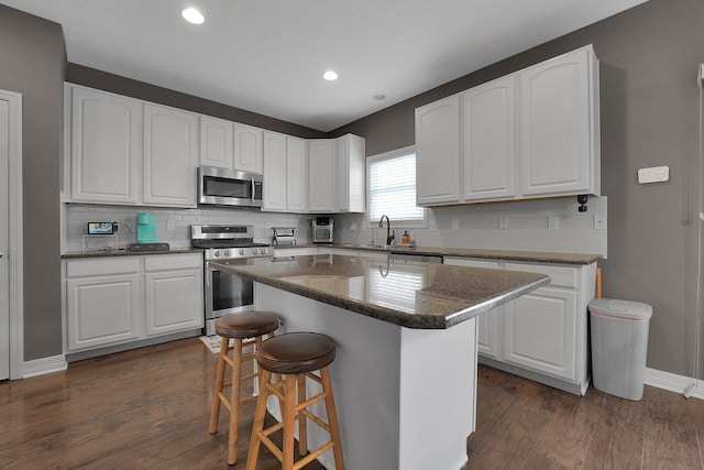 kitchen with dark wood finished floors, a kitchen bar, stainless steel appliances, and a sink