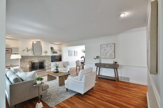 living area with a stone fireplace, baseboards, wood finished floors, and visible vents