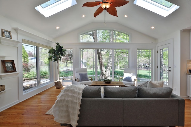 living area with vaulted ceiling with skylight, light wood finished floors, a ceiling fan, and recessed lighting