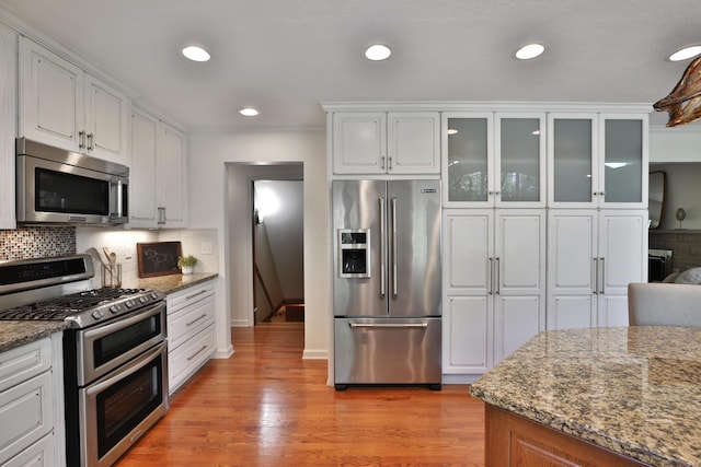 kitchen with decorative backsplash, light wood-style flooring, white cabinets, stone counters, and appliances with stainless steel finishes