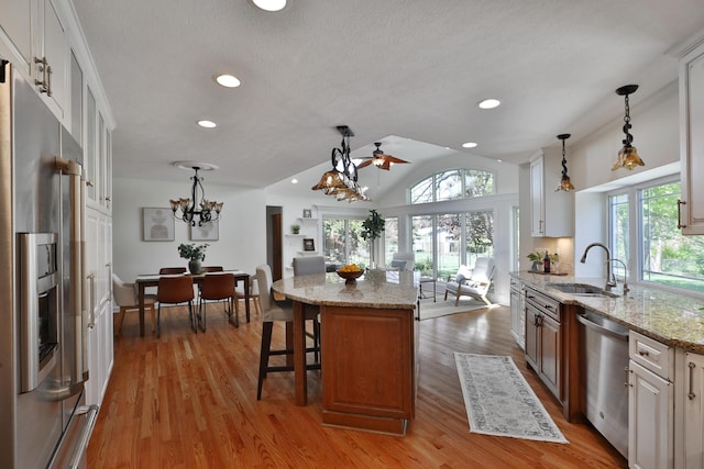 kitchen featuring lofted ceiling, light stone countertops, a sink, hanging light fixtures, and stainless steel appliances