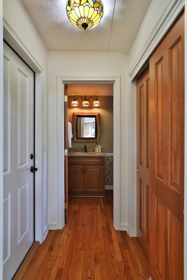 corridor featuring baseboards, a sink, and dark wood-style floors