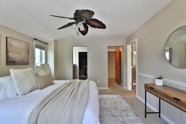 bedroom with light carpet, baseboards, ceiling fan, a textured ceiling, and a spacious closet