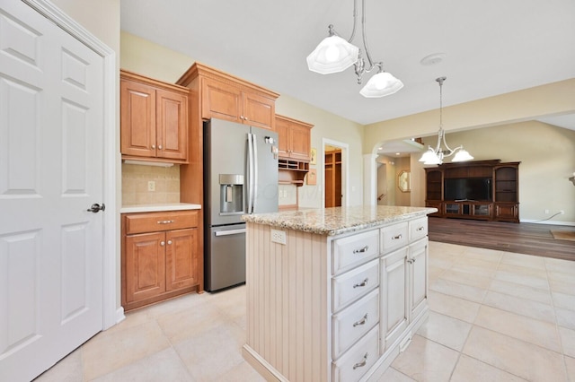kitchen featuring decorative backsplash, a kitchen island, arched walkways, decorative light fixtures, and stainless steel fridge