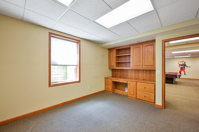 unfurnished office featuring a paneled ceiling, built in study area, carpet floors, and baseboards