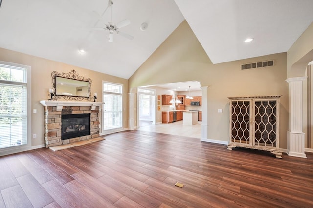 unfurnished living room featuring wood finished floors, a stone fireplace, visible vents, a ceiling fan, and high vaulted ceiling