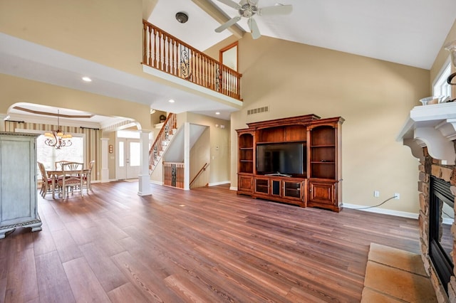 unfurnished living room featuring decorative columns, ceiling fan with notable chandelier, a fireplace, visible vents, and high vaulted ceiling