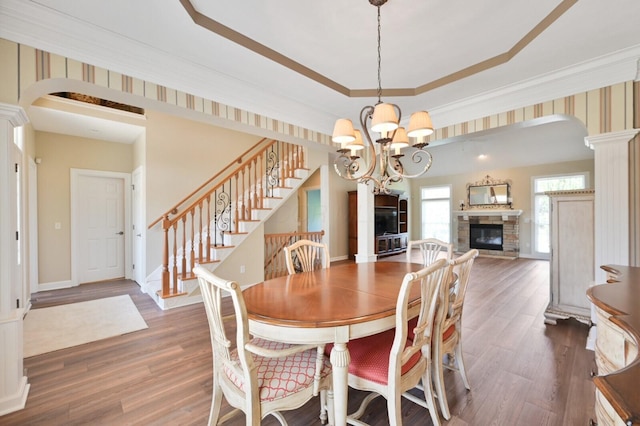dining area with arched walkways, a stone fireplace, a chandelier, and wood finished floors