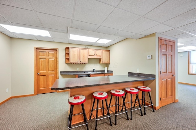 kitchen featuring a sink, a peninsula, carpet, baseboards, and dark countertops