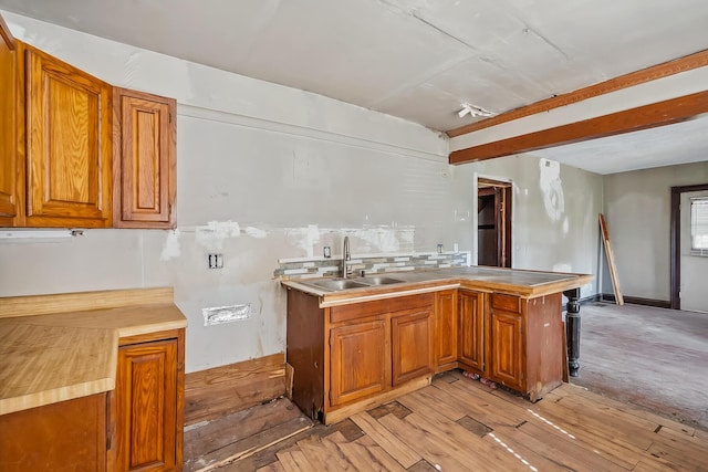 kitchen with brown cabinets, a sink, light countertops, beam ceiling, and light wood finished floors