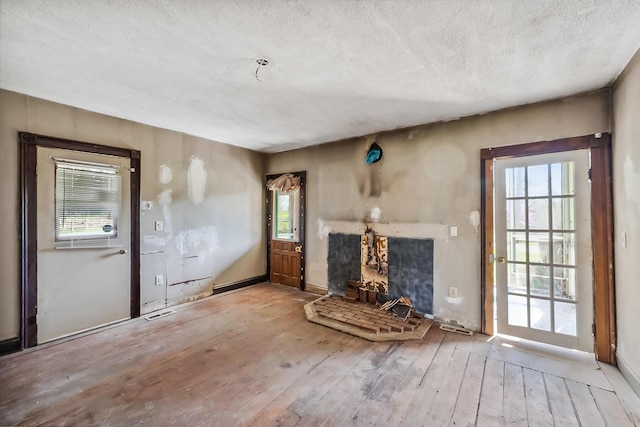 unfurnished living room featuring a fireplace with raised hearth, wood-type flooring, baseboards, visible vents, and a textured ceiling
