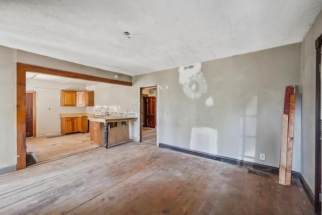 unfurnished living room with light wood-type flooring, a sink, baseboards, visible vents, and a textured ceiling