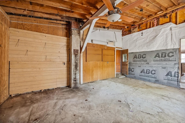 miscellaneous room with wood walls, ceiling fan, and unfinished concrete flooring