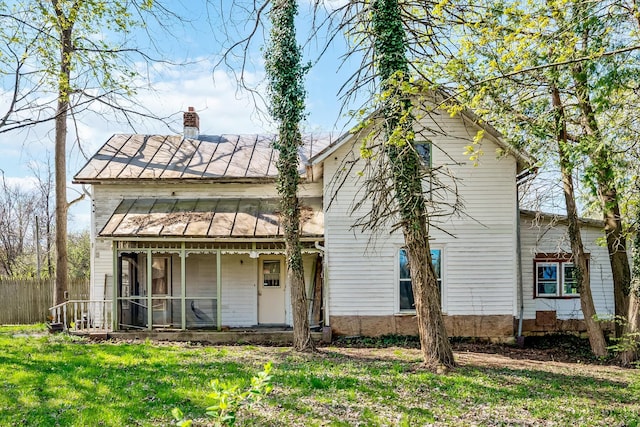 rear view of house with a standing seam roof, metal roof, a yard, a chimney, and fence