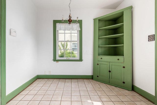 unfurnished dining area featuring baseboards, light tile patterned flooring, and a chandelier