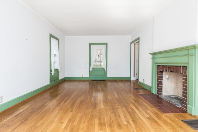 unfurnished living room with a brick fireplace, baseboards, wood finished floors, visible vents, and ornamental molding