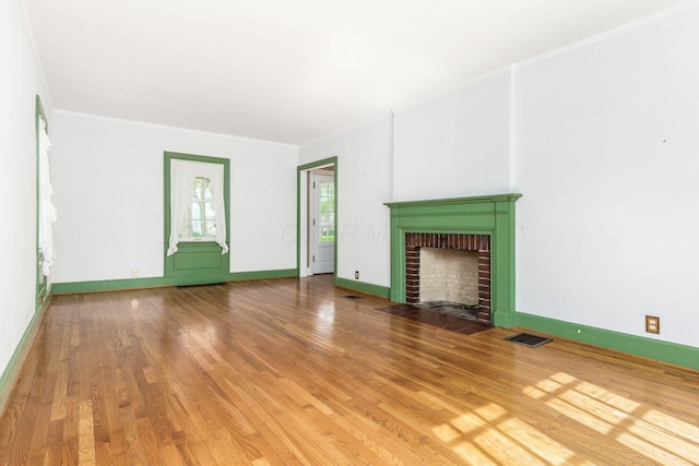 unfurnished living room with a fireplace, baseboards, wood finished floors, visible vents, and ornamental molding