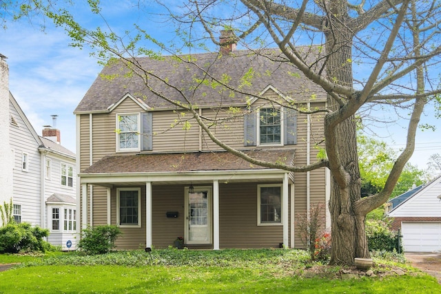 traditional-style house featuring a garage, a front yard, a chimney, and covered porch
