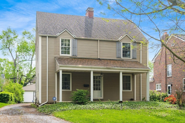 traditional-style house with a garage, a front lawn, a chimney, a porch, and an outbuilding