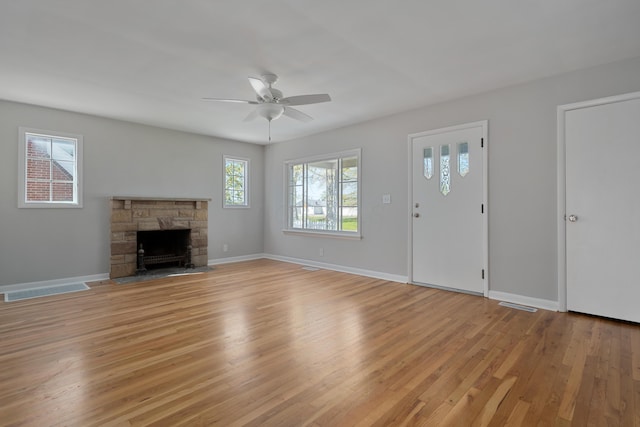 unfurnished living room featuring light wood finished floors, baseboards, visible vents, ceiling fan, and a stone fireplace