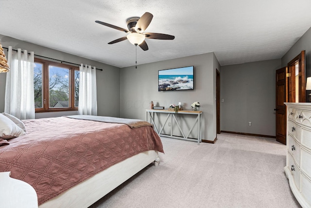 bedroom featuring light colored carpet, baseboards, ceiling fan, and a textured ceiling