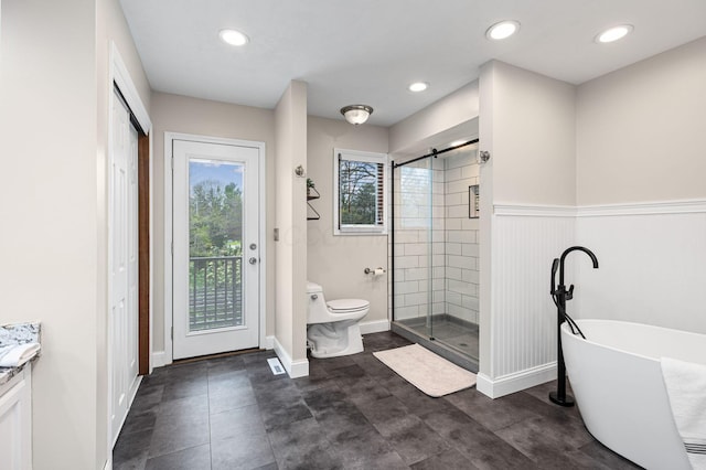 bathroom with a stall shower, toilet, a soaking tub, wainscoting, and recessed lighting