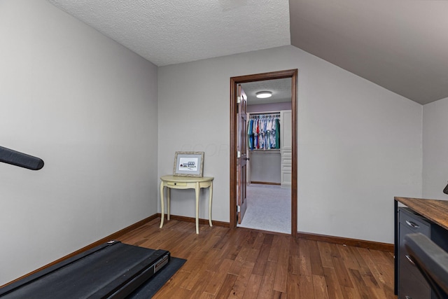 exercise room with dark wood finished floors, baseboards, vaulted ceiling, and a textured ceiling