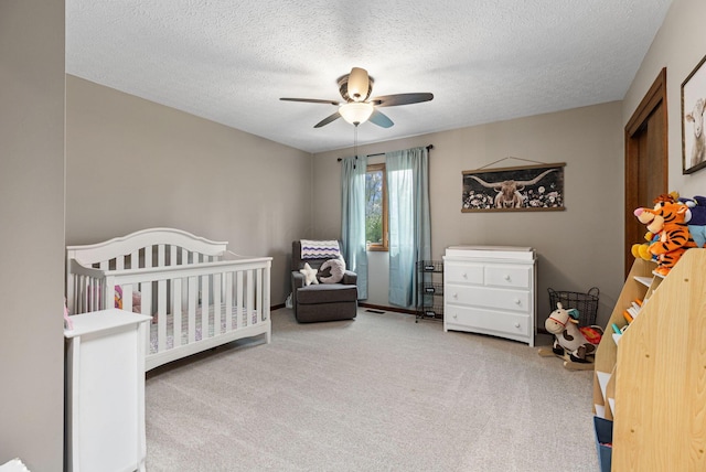 bedroom with carpet floors, a crib, a textured ceiling, and a ceiling fan