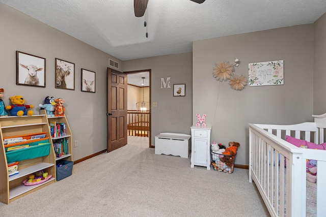 bedroom with a crib, carpet floors, a textured ceiling, baseboards, and a ceiling fan