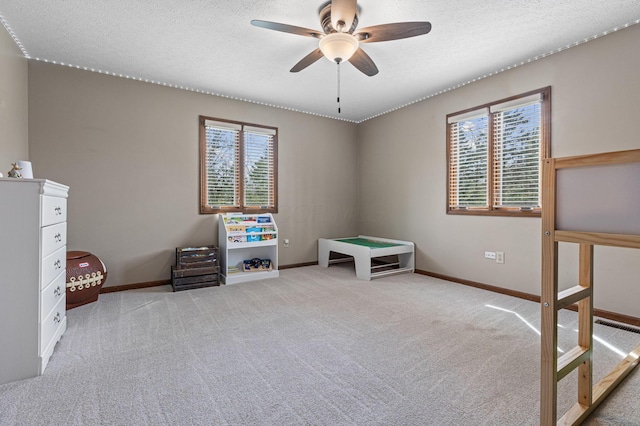 unfurnished bedroom featuring multiple windows, baseboards, carpet flooring, a textured ceiling, and a ceiling fan