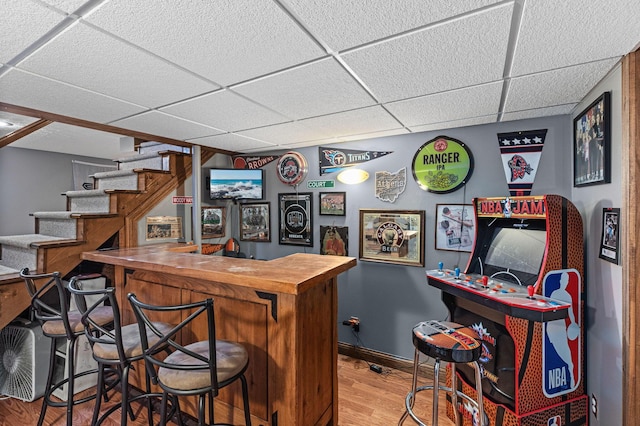 indoor bar featuring a drop ceiling, stairs, wood finished floors, and baseboards