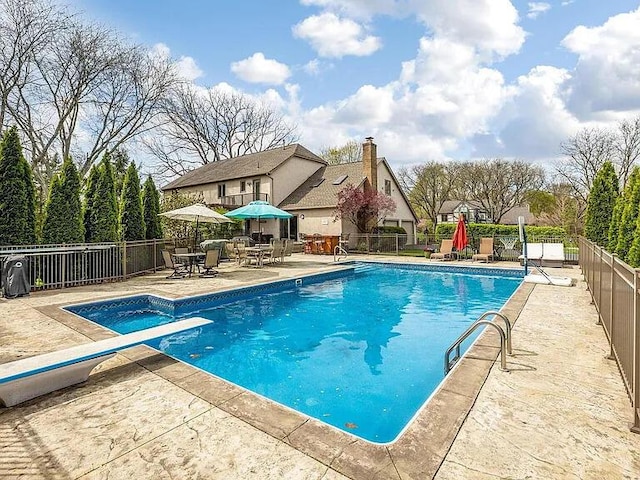 view of swimming pool with a patio, a fenced backyard, outdoor dining space, and a diving board