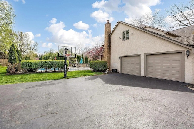 view of home's exterior with asphalt driveway, a garage, stucco siding, a lawn, and a chimney