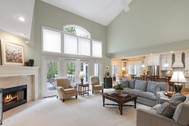 living area with a tiled fireplace, high vaulted ceiling, plenty of natural light, and light colored carpet