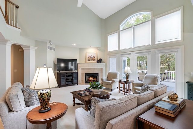 living area featuring visible vents, carpet floors, a lit fireplace, high vaulted ceiling, and ornate columns