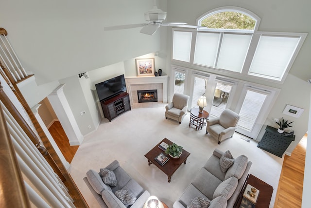 living room with a ceiling fan, a towering ceiling, wood finished floors, and a fireplace