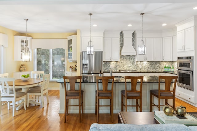 kitchen with dark countertops, light wood finished floors, stainless steel appliances, backsplash, and custom exhaust hood