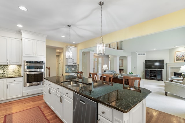 kitchen with decorative columns, a kitchen island with sink, open floor plan, a sink, and stainless steel appliances